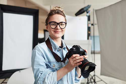Female photographer holding camera in a studio.