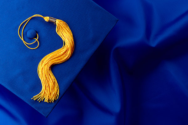 Blue mortarboard and yellow tassel shot on blue graduation gown