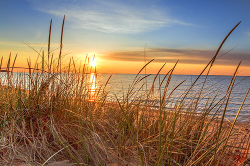 Sunrise illuminates sand dunes and the blue water horizon