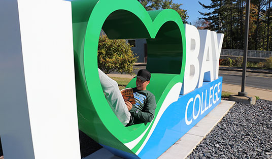 Bay College student reading outside on the Iron Mountain campus.