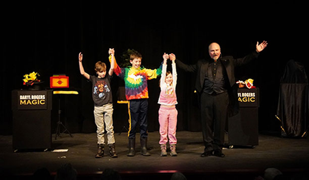 Daryl Rogers on stage with three young audience members