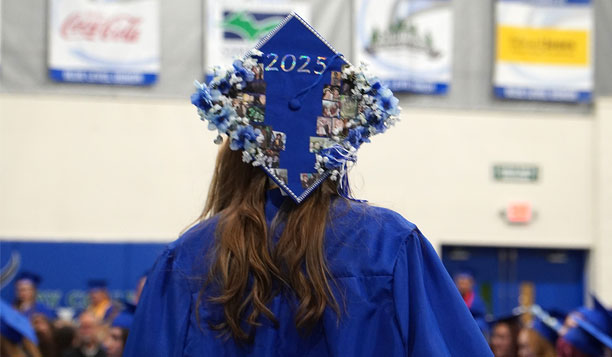 Woman shown from behind wearing a graduation cap and gown in 2025. The cap has flowers on it and the year.
