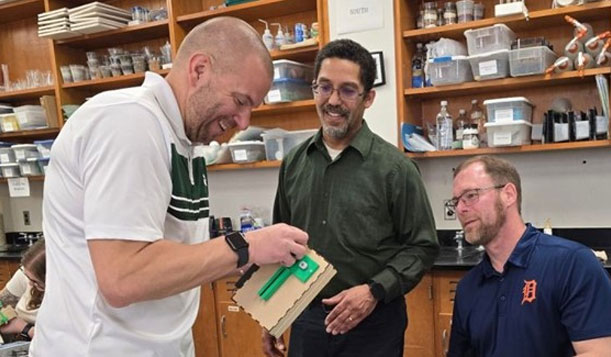 Professors Matt Oney and David Ramsey support a workshop participant in their build of a paper airplane launcher.