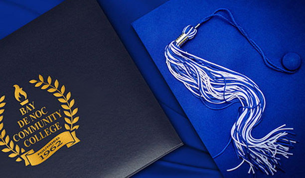 Bay College gold embossed diploma case and bright blue grad cap and tassel.