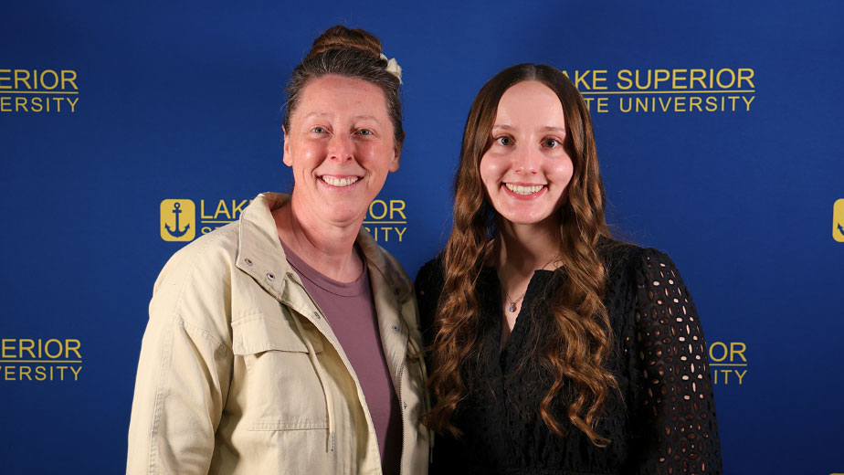 : LSSU Regional Center Director Heidi Rife smiles beside Lukenda School of Business Outstanding Regional Center Student Allyson Lancour, in front of a Lake Superior State University logo backdrop.